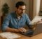 Pessoa em casa, sentada à mesa, digitando no laptop enquanto segura uma certificação, com outras certificações sobre a mesa e ambiente iluminado de forma natural