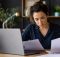 Uma mulher concentrada organiza documentos e revisa informações em um notebook, em um ambiente de trabalho moderno e bem iluminado